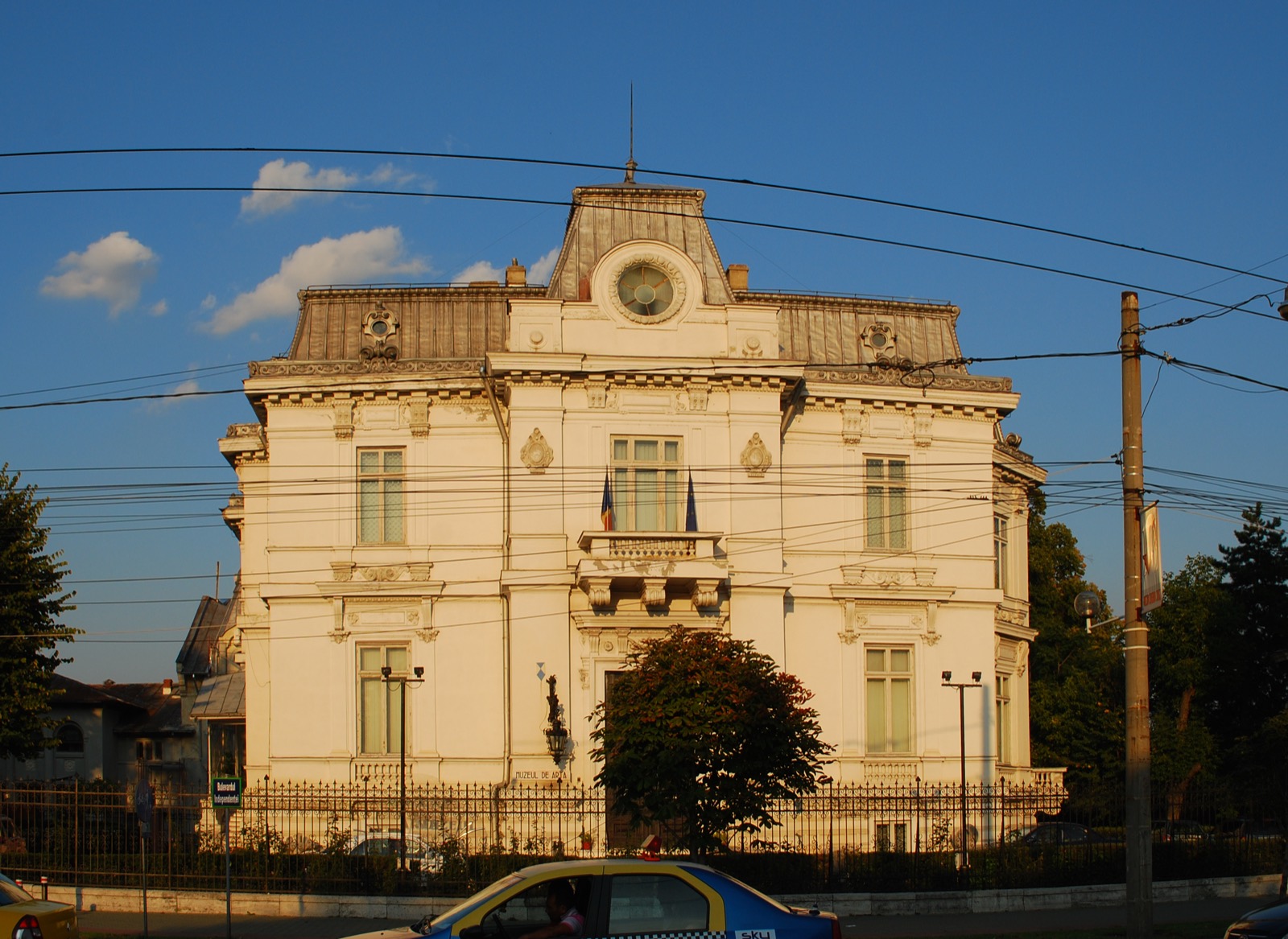 Fațada palatului în lumina caldă a după-amiezii târzii, cu steaguri la balcon, văzută de pe bulevard