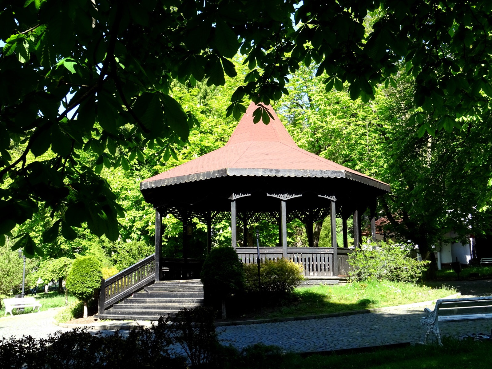 Foișorul de lemn cu acoperiș roșu din parc, între castani