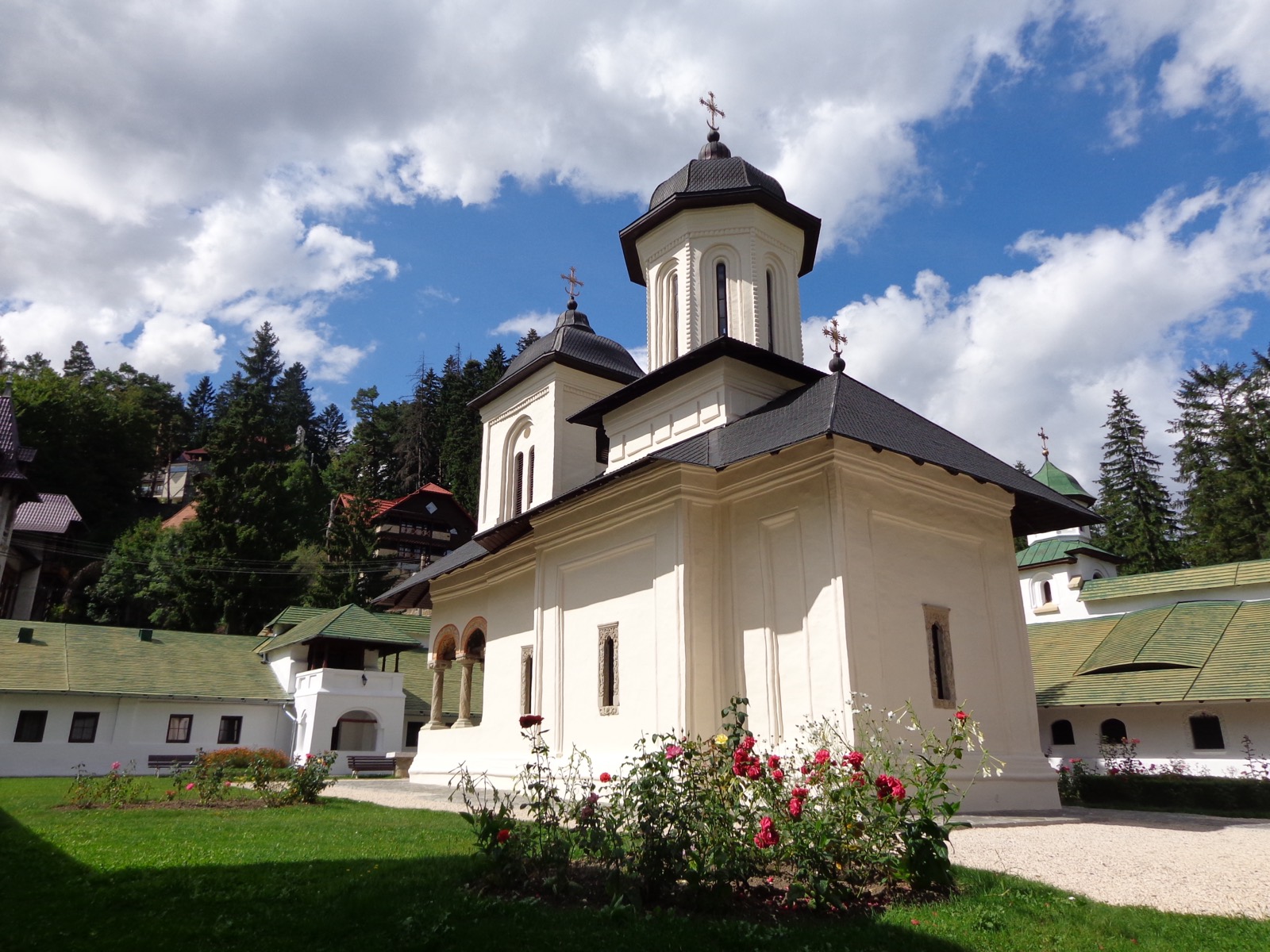 Biserica veche „Adormirea Maicii Domnului”, albă, cu două turle și trandafiri în fața ei, în curtea veche